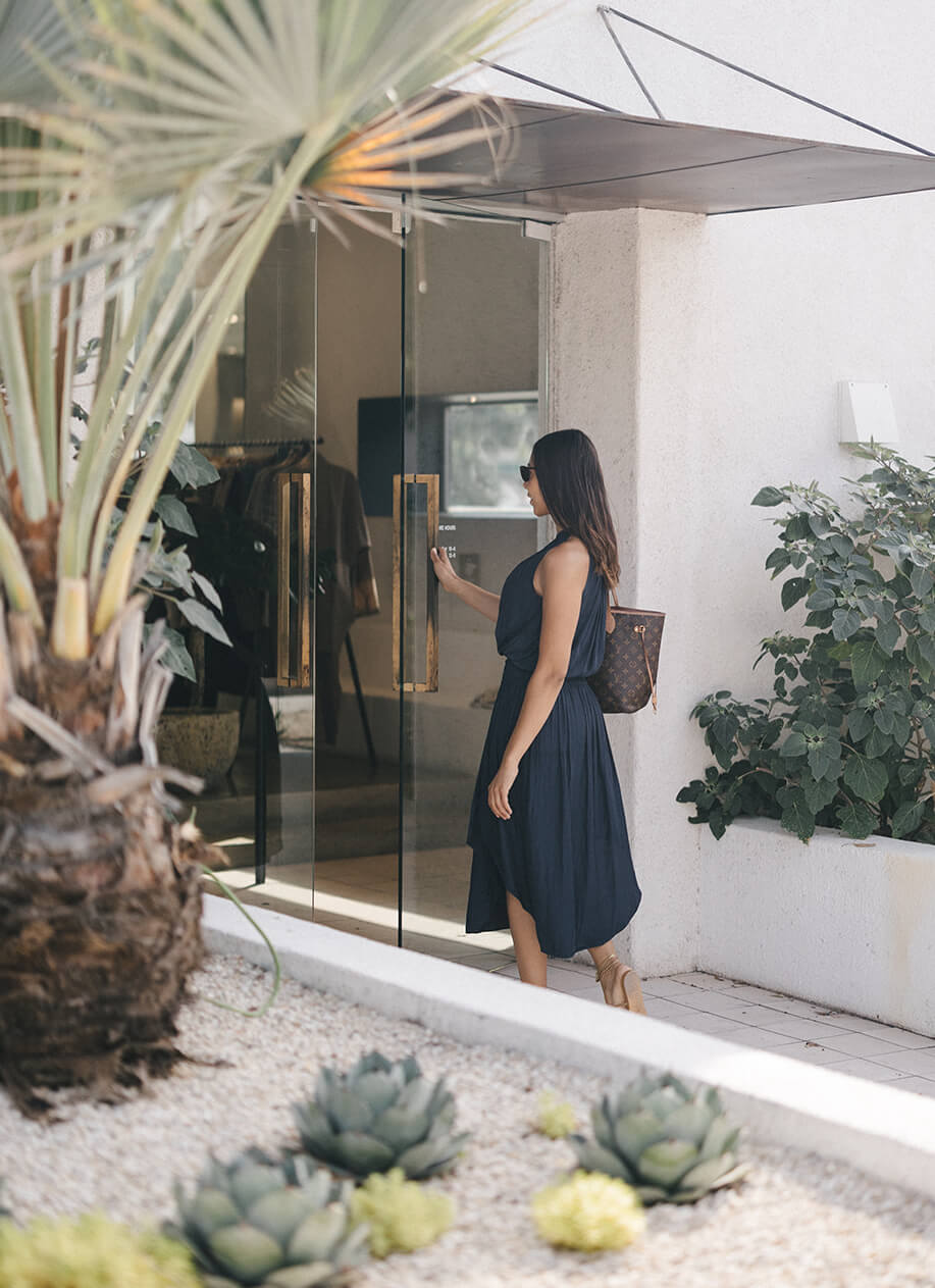 Customer entering the Kick Pleat store in Austin, a boutique with a modern and minimalist entrance, framed by lush greenery.