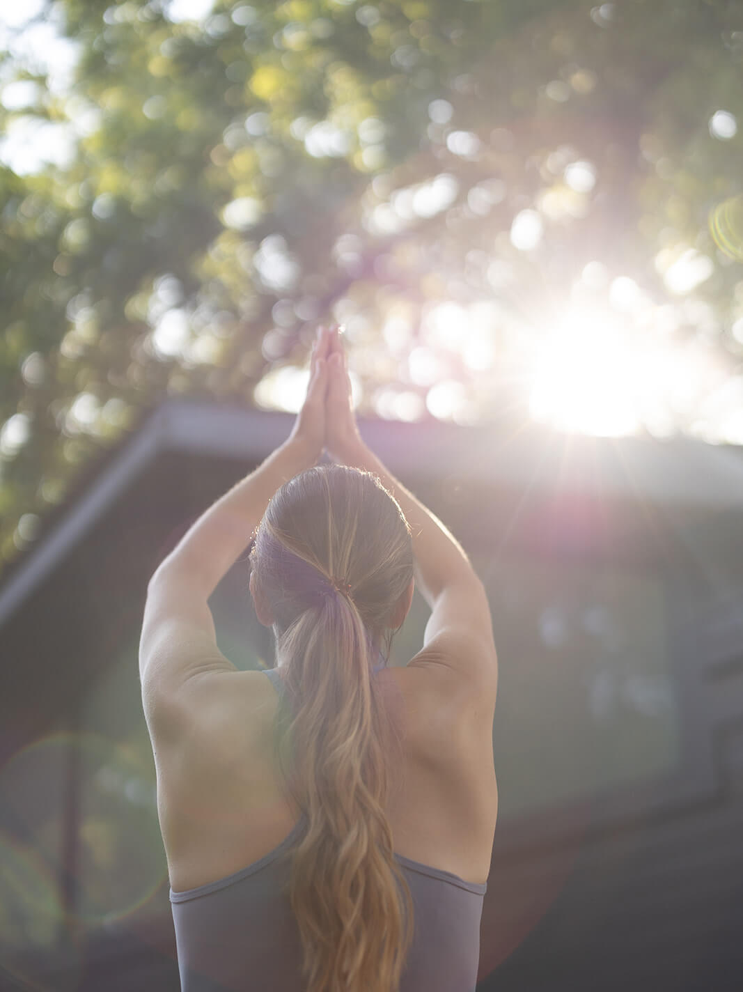 Woman practicing yoga in a serene outdoor environment with sunlight filtering through the trees.