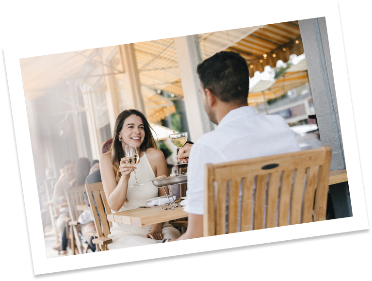 a couple dining outside at a wooden table drinking white wine.