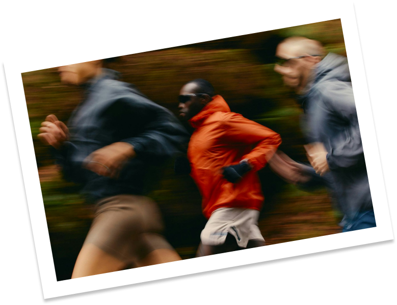 A group of 3 men running outdoors on a trail with windbreakers on. The picture is a little blurry to dictate movement.