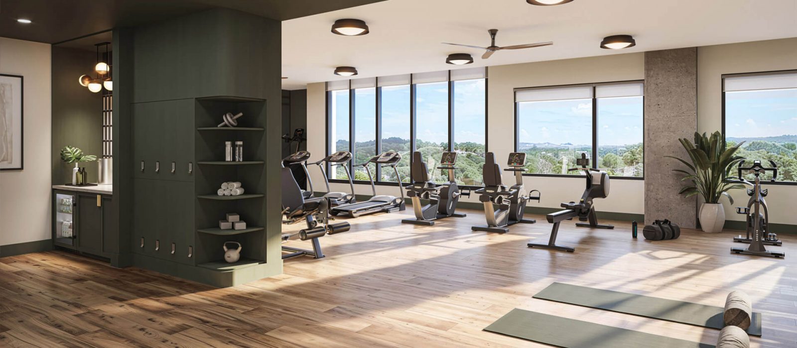 Well-equipped fitness center with cardio machines, a bright open space, wooden floors, and large windows offering scenic views of the outdoors.