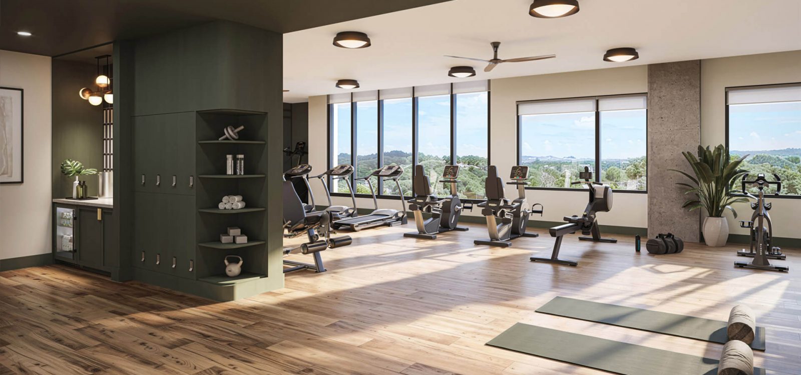 Well-equipped fitness center with cardio machines, a bright open space, wooden floors, and large windows offering scenic views of the outdoors.